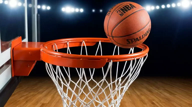 Single orange basketball mid-flight just before it passes through a hoop with a white net on an indoor hardwood court