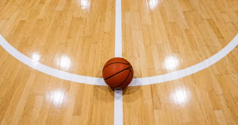 Orange basketball on a hardwood court next to white painted three-point line and free-throw line in sharp focus